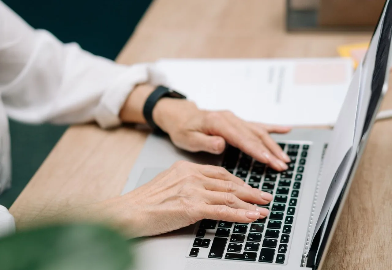 Hands typing on a laptop keyboard on a white desk in an office
